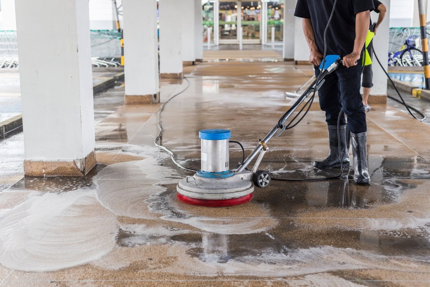 Person using a floor scrubber to clean a wet concrete floor in a parking structure
