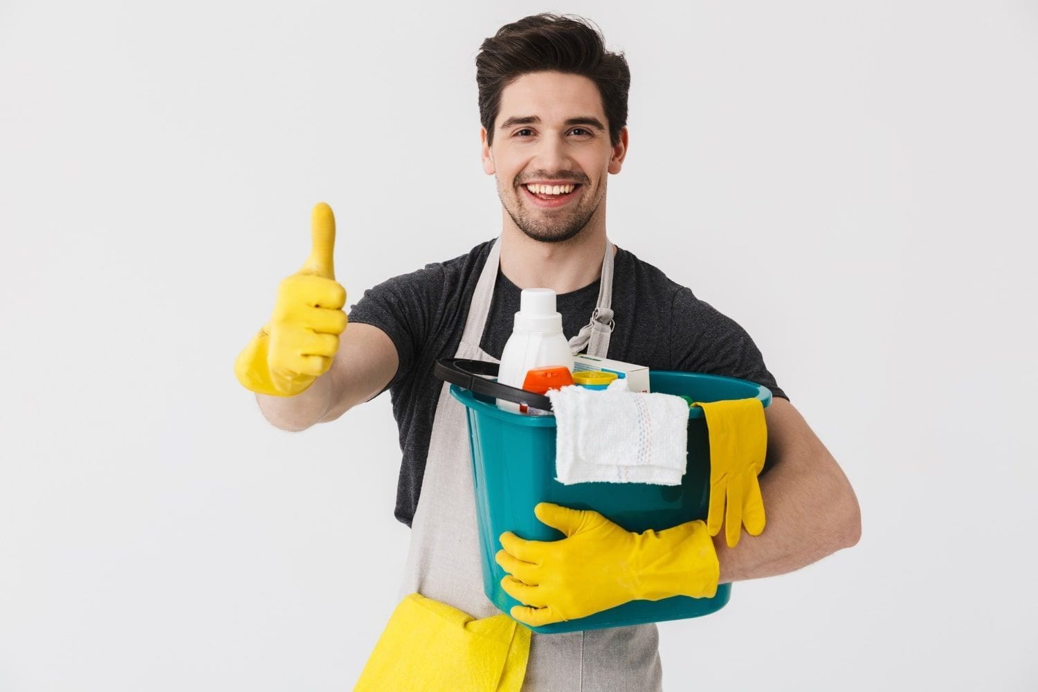 Smiling cleaner in yellow gloves holding cleaning supplies and giving a thumbs-up