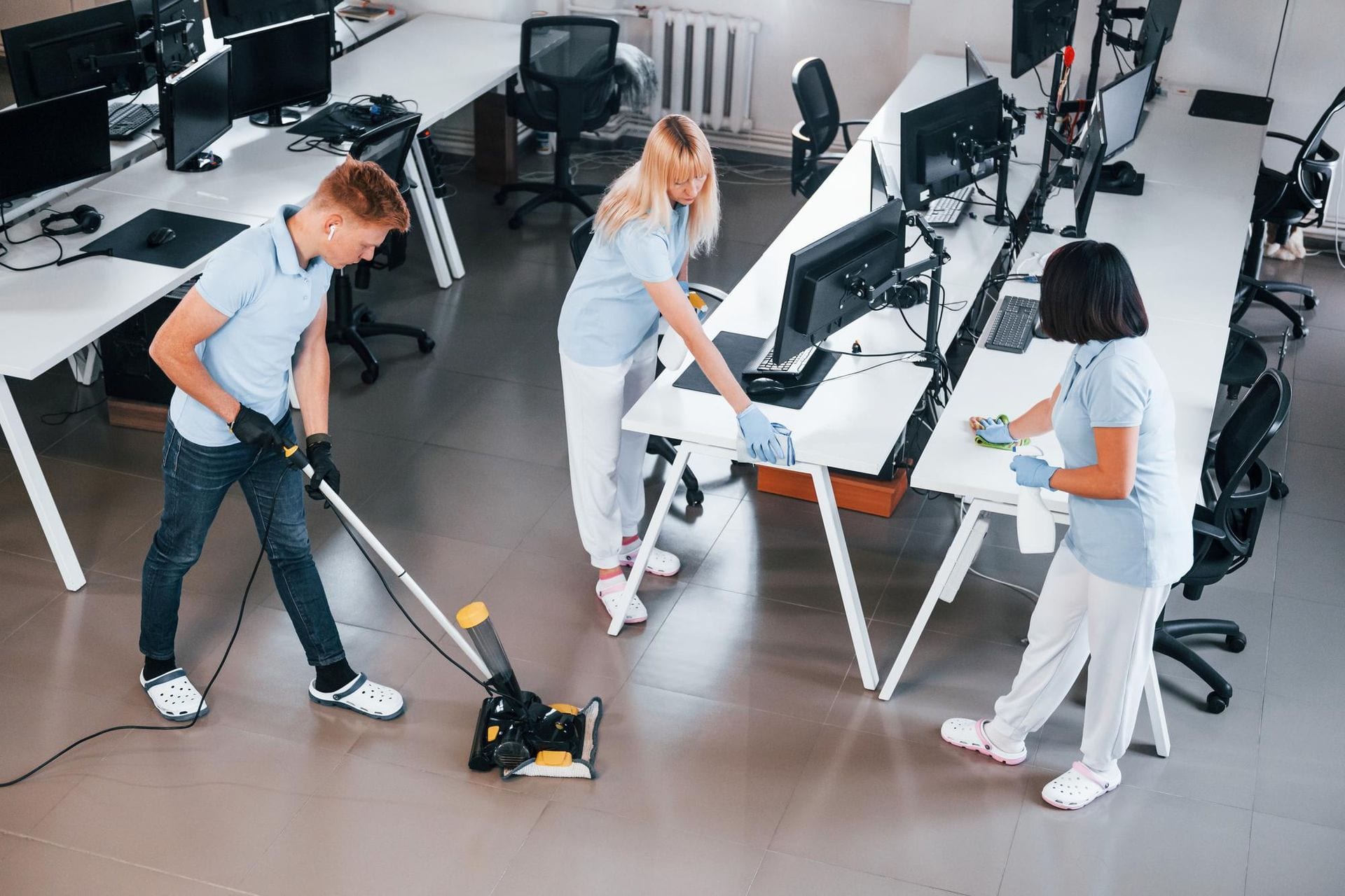 Person in protective suit spraying disinfectant in a classroom with desks and chairs.