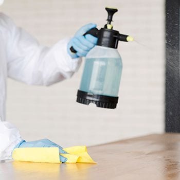 Gloved hand using a spray bottle beside yellow cloth on a table during cleaning